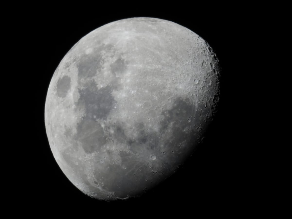 A black and white image of the moon, three-quarters illuminated. 