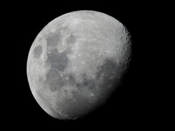 A black and white image of the moon, three-quarters illuminated. 